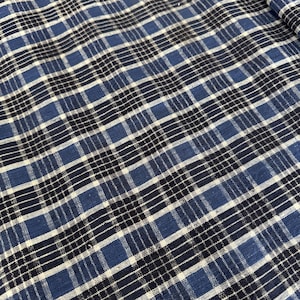 Peut inclure: Un tissu tissé présentant un motif à carreaux composé de lignes entrecroisées dans des tons de bleu foncé, bleu moyen et blanc. Le textile affiche un design à grille cohérent avec des rayures alternées épaisses et fines formant un motif carré.