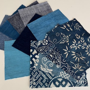 May include: A collection of rectangular fabric swatches in various shades of blue, ranging from light turquoise to deep navy. Several pieces feature intricate white botanical and geometric patterns, while others are solid-colored textured textiles.