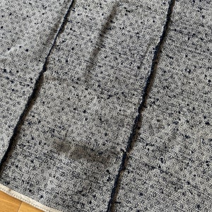 May include: Close-up of a woven fabric with a white background and black speckles. The fabric has a textured, slightly rough surface.