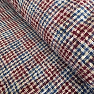 Op de afbeelding: Close-up van een stoffen rol met een klassiek ruitpatroon. De stof heeft een herhalend ruitontwerp in bordeauxrood, blauw en gebroken wit. Het materiaal lijkt geweven te zijn, met een licht getextureerd oppervlak.