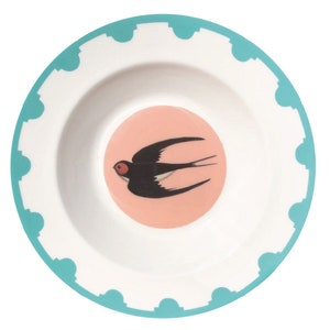 May include: White ceramic bowl with a teal scalloped rim and a pink center. The center features a black swallow bird with a red eye. The bowl is designed for serving food.