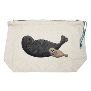Puede incluir: Una bolsa con cremallera de lona con una foca gris oscuro con manchas negras y una cría de foca marrón claro. Las focas están tumbadas. La bolsa tiene una cremallera dorada y un cordón turquesa.