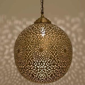 Może przedstawiać: Mosiężna, kulista lampa wisząca z misternymi ażurowymi wzorami. Lampa zawieszona na łańcuchu rzuca dekoracyjne cienie. Emituje ciepłą poświatę. Średnica ok. 30 cm.