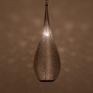 May include: A teardrop-shaped pendant light fixture with a textured, perforated metal shade. The light fixture is suspended from a chain and emits a warm glow. The shade has a bronze finish and is covered in small, evenly spaced holes.