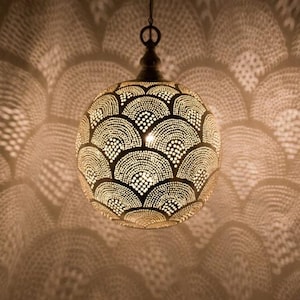 May include: A decorative, spherical pendant light with a detailed, openwork design. The light casts a patterned shadow on the wall. The fixture is made of metal and has a warm, inviting glow, perfect for home decor.