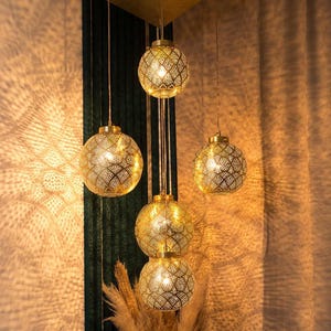 May include: A cluster of five gold-colored, spherical pendant lights with intricate, patterned cutouts. The lights are suspended from the ceiling, casting decorative light patterns on the surrounding walls. The warm glow creates a cozy ambiance.