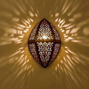 May include: A decorative wall sconce with a warm, inviting glow. The sconce has a dark brown, diamond-shaped frame with intricate cut-out patterns. The light casts a beautiful pattern on the wall, creating a cozy ambiance. This fixture is ideal for adding a touch of elegance to any space.