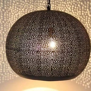May include: A dark, spherical pendant light with a perforated design, casting a dotted pattern on the wall. The light fixture is suspended from a chain, creating a warm, ambient glow. The lamp's diameter is approximately 12 inches.