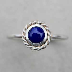Könnte beinhalten: Ein silberner Ring mit einem blauen Edelstein, der in einem seilartigen Design gefasst ist.