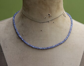 May include: A necklace made of small, light blue gemstone beads. The necklace is displayed on a fabric-covered mannequin.