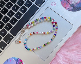 Op de afbeelding: Een veelkleurige kralenketting met witte parels. De ketting ligt op een zilveren laptop.