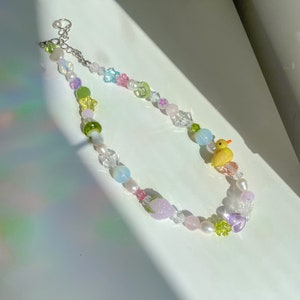 May include: A colorful beaded necklace with a yellow rubber duck charm, green, pink, and purple beads, and a silver chain.