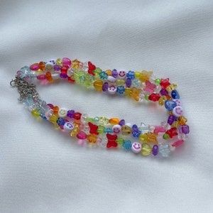 May include: Multi-coloured beaded necklace with smiley face, butterfly and star charms. The necklace is made of clear, red, yellow, blue, green and purple beads.