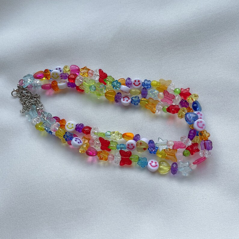 May include: Multi-coloured beaded necklace with smiley face, butterfly and star charms. The necklace is made of clear, red, yellow, blue, green and purple beads.