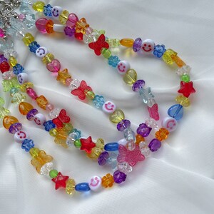 May include: Multicoloured beaded necklace with smiley face, star, butterfly and flower charms. The necklace is made of plastic beads and is layered with multiple strands.