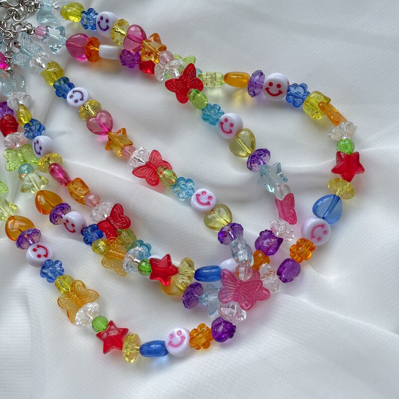 May include: Multicoloured beaded necklace with smiley face, star, butterfly and flower charms. The necklace is made of plastic beads and is layered with multiple strands.