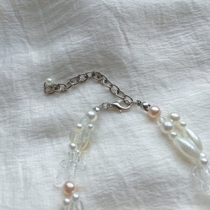 Peut inclure: Un collier de perles blanches et roses avec un fermoir et une cha&icirc;ne argent&eacute;s. Le collier est compos&eacute; de plusieurs rangs de perles et de perles.