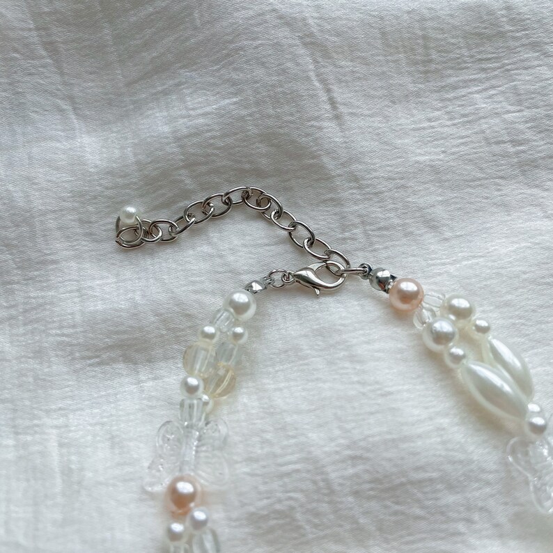 Peut inclure: Un collier de perles blanches et roses avec un fermoir et une cha&icirc;ne argent&eacute;s. Le collier est compos&eacute; de plusieurs rangs de perles et de perles.