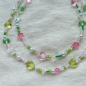 Puede incluir: Un collar delicado con cuentas rosas, verdes y blancas. Las cuentas est&aacute;n dispuestas en un patr&oacute;n de corazones, flores y peque&ntilde;as cuentas redondas. El collar est&aacute; hecho de un hilo delgado y es perfecto para superponer.