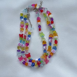 May include: Multi-layered necklace featuring colourful beads, including butterflies, stars, hearts, and smiley faces. The necklace is made of plastic and has a silver chain.