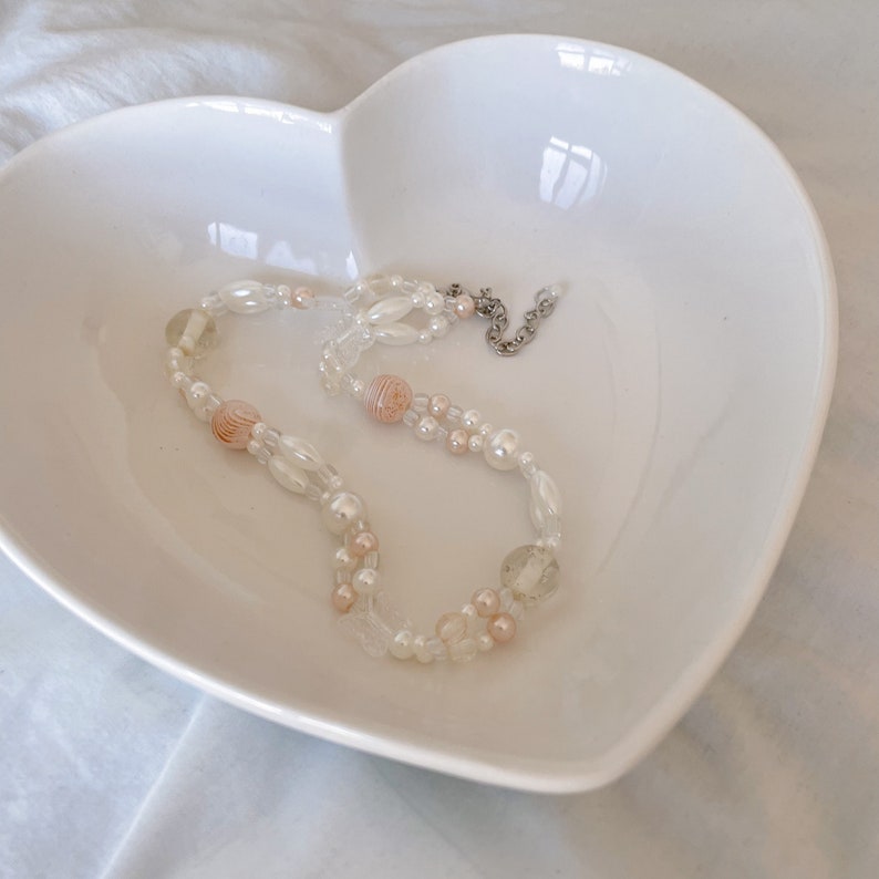 Peut inclure: Un plat en forme de c&oelig;ur blanc contenant un collier de perles d&eacute;licates blanches et roses.