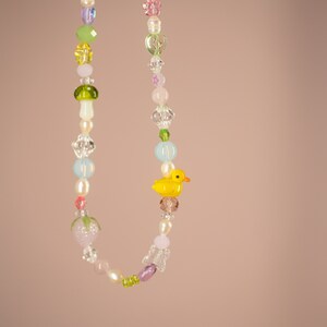 May include: A colorful beaded necklace with a yellow rubber duck charm. The necklace features various shapes and sizes of beads, including hearts, stars, and mushrooms.