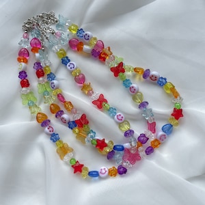 May include: Three colourful beaded necklaces with butterfly and smiley face charms. The necklaces are made of clear plastic beads in shades of red, orange, yellow, green, blue, and purple.