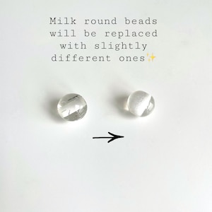 May include: Two clear, round beads on a white background. The bead on the left has internal lines, while the bead on the right has a white, glittery section. Text above reads: "Milk round beads will be replaced with slightly different ones."