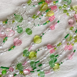 Puede incluir: Un collar de cuentas multicadena con cuentas de coraz&oacute;n de color rosa, verde y blanco. El collar est&aacute; hecho de varios materiales, incluyendo vidrio, pl&aacute;stico y perla.