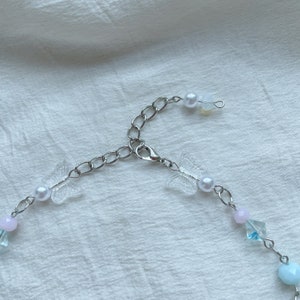 Pode incluir: Um delicado colar de corrente prateada com fecho de lagosta. O colar apresenta pingentes de borboleta de pl&aacute;stico transparente, contas de p&eacute;rola branca e contas de cristal azul claro e rosa.