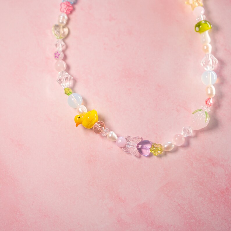 May include: A colorful beaded necklace with a yellow duck charm, pink and white beads, and a clear crystal butterfly charm.