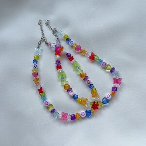 May include: Three colourful beaded necklaces with butterfly and smiley face charms. The necklaces are made with clear, red, yellow, blue, green, and pink beads.