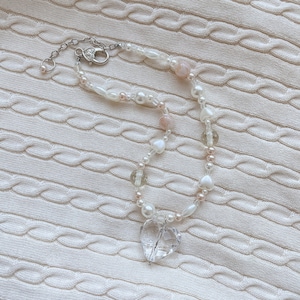 May include: A necklace with a clear heart pendant, strung with white pearls, clear beads, and small pink beads. The silver-toned clasp secures the necklace. The jewellery is displayed on a white, textured background.