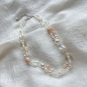 Peut inclure: Un collier d&eacute;licat &agrave; double rang de perles blanches et roses, comprenant des perles nacr&eacute;es et des breloques papillon transparentes.