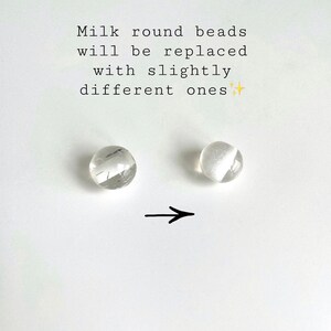 Peut inclure: Deux perles rondes transparentes, l'une avec une finition plus opaque que l'autre. Une fl&egrave;che pointe de la perle la plus opaque vers la perle la moins opaque. Le texte "Milk round beads will be replaced with slightly different ones" est au-dessus des perles.