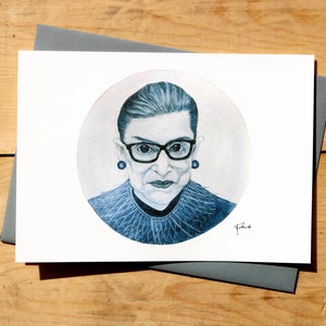 May include: A blue and white illustration of Ruth Bader Ginsburg, a Supreme Court Justice, wearing glasses and a lace collar. The illustration is in a circle on a white background.