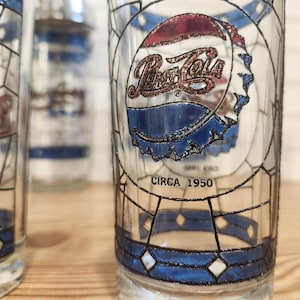 May include: Vintage Pepsi-Cola glasses with a stained-glass design. The glasses feature the Pepsi-Cola logo and a bottle cap design in red, white, and blue. The text "CIRCA 1950" is printed on the glass. The glasses have a geometric pattern.