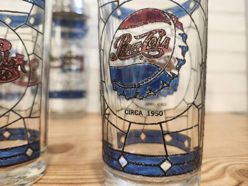 May include: Vintage Pepsi-Cola glasses with a stained-glass design. The glasses feature the Pepsi-Cola logo and a bottle cap design in red, white, and blue. The text "CIRCA 1950" is printed on the glass. The glasses have a geometric pattern.