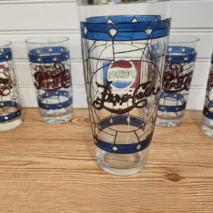 May include: Set of five vintage Pepsi-Cola glasses. Each glass features a stained-glass design with blue, white, and red accents. The Pepsi logo is prominently displayed on each glass, making them a collectible item.