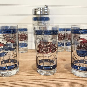 May include: A set of vintage Pepsi Cola glasses and a cocktail shaker. The glasses feature a stained-glass design with the Pepsi logo and the text "Circa 1962" and "Circa 1950". The cocktail shaker is stainless steel with blue stripes.