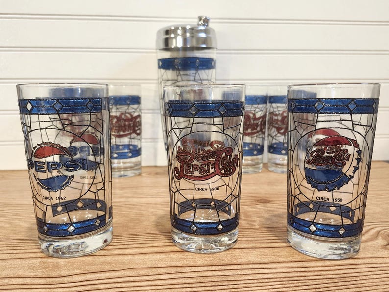 May include: A set of vintage Pepsi Cola glasses and a cocktail shaker. The glasses feature a stained-glass design with the Pepsi logo and the text "Circa 1962" and "Circa 1950". The cocktail shaker is stainless steel with blue stripes.