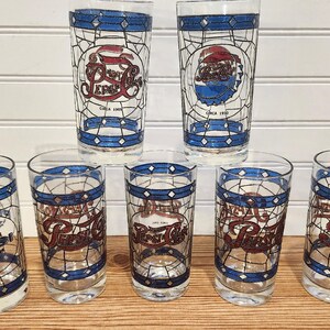 May include: A set of seven vintage Pepsi Cola glasses. Each glass features a stained-glass style design with the Pepsi logo in red, white, and blue. The glasses have a blue border and the text "Circa 1950".
