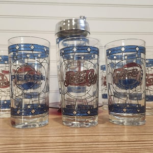 May include: Set of six vintage Pepsi Cola glasses with a blue and white stained glass design. Each glass features the Pepsi logo in red and blue, with the text "Chicago 1902". A stainless steel cocktail shaker is in the background.