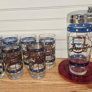 May include: A vintage Pepsi-Cola cocktail shaker and glasses set. The clear glasses and shaker feature a stained-glass design with blue and red accents. The set includes a shaker, a coaster, and six glasses.
