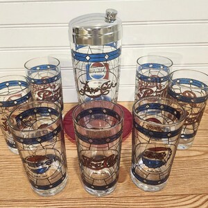 May include: A vintage Pepsi-Cola cocktail shaker and glasses set. The clear glasses and shaker feature a stained-glass design with the Pepsi logo in red, white, and blue. The set includes a metal-topped shaker and six glasses.