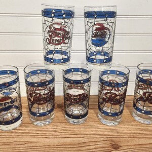 May include: Set of seven vintage Pepsi cola glasses. Each glass features a stained-glass style design with the Pepsi logo in red, white, and blue. The glasses have a blue band around the rim and base, with the words "Circa 1990".