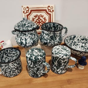 May include: A collection of enamelware kitchen items with a white and dark green speckled pattern. The set includes a lidded pot, mugs, a bowl, and salt and pepper shakers. A decorative ceramic tile and a small chicken figurine are also present.