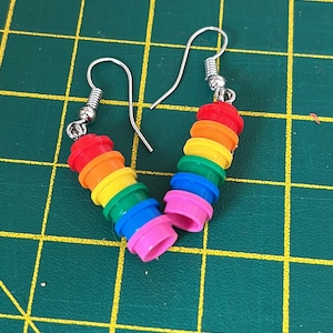 Op de afbeelding: Een paar regenboogkleurige oorbellen gemaakt van gestapelde Lego-stenen. De oorbellen zijn zilver en hebben een haaksluiting.