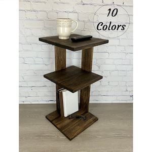 Könnte beinhalten: Ein dunkelbrauner, dreistufiger Beistelltisch aus Holz mit quadratischer Oberseite und Ablagen. Eine weiße Tasse, eine Fernbedienung, Bücher und eine Brille liegen auf den Ablagen. Der Text "10 Farben" ist enthalten.