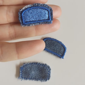Puede incluir: Tres pequeños parches de tela similar al denim con costuras azules. Uno es rectangular, los otros dos son arqueados. Los parches tienen un borde deshilachado, lo que les da un aspecto rústico. Estos parches podrían usarse para reparar o decorar ropa.